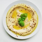 overhead of hummus in a white bowl with basil garnish