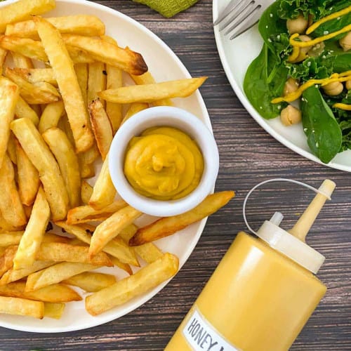 Bottle of vegan honey mustard next to fries and salad.