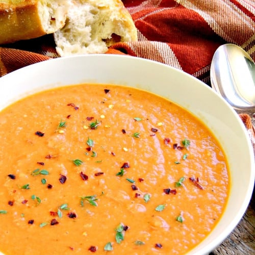 Creamy tomato soup in a bowl with a spoon and bread.