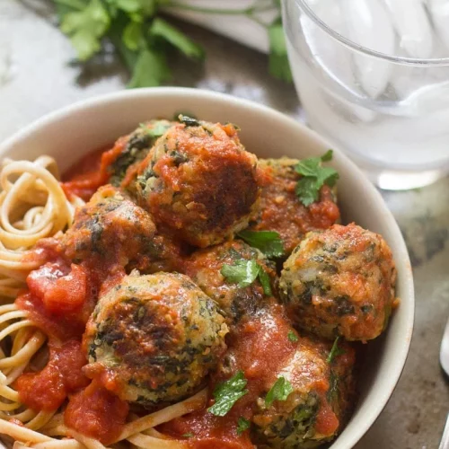 Cannellini bean broccoli rabe meatballs in a bowl next to a glass of ice water.