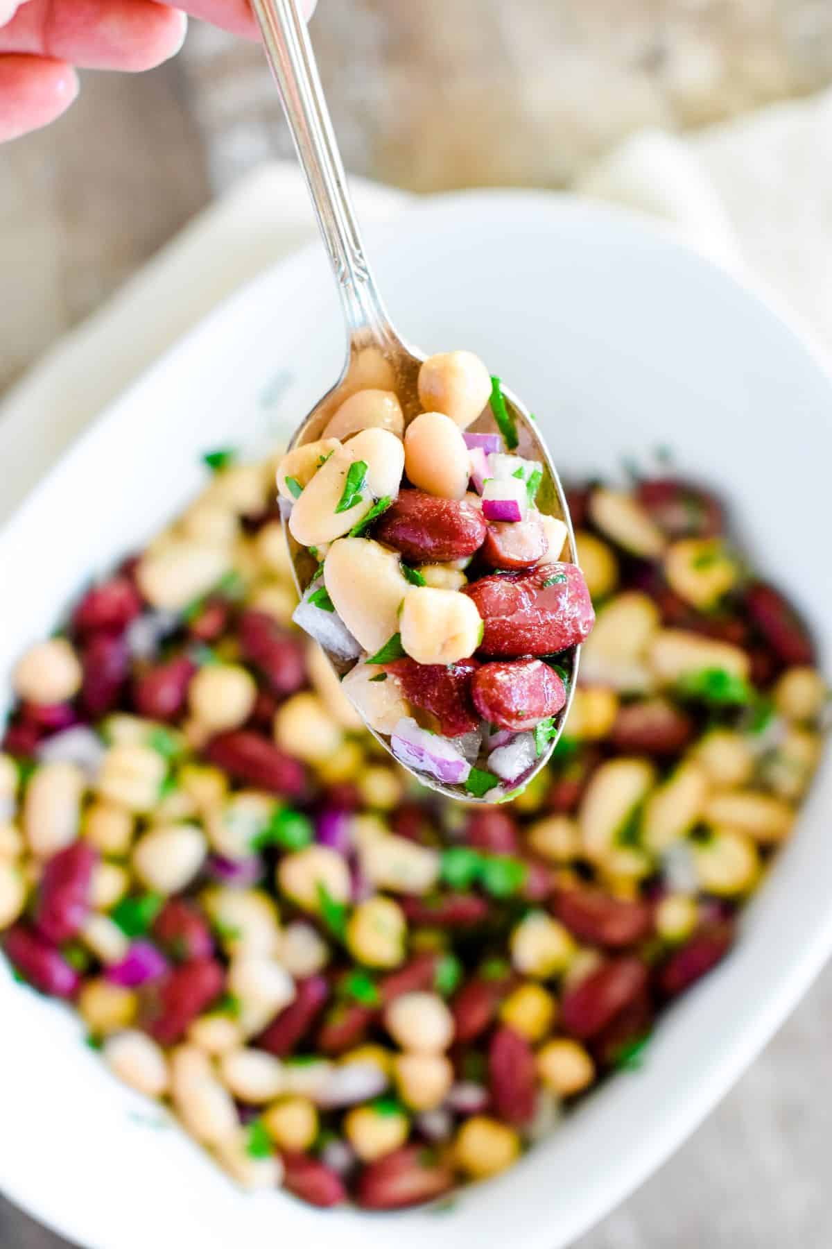 close-up of spoonful of bean salad over the rest of it in a white serving dish.