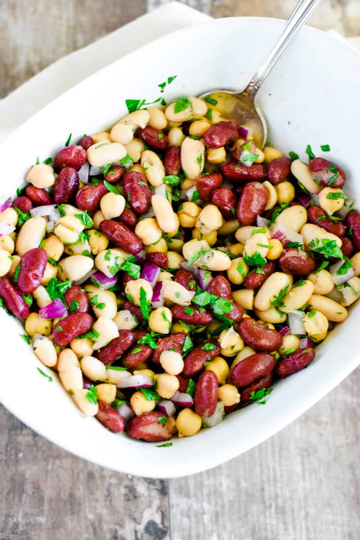 bean salad in white serving dish after being mixed with a spoon in it.