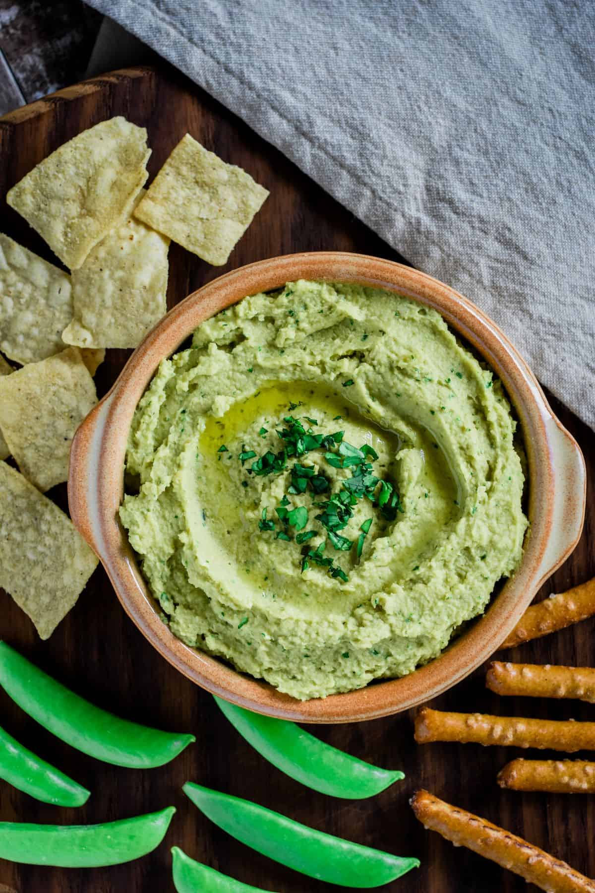overhead of avocado hummus in a bowl with dipping snacks around it.