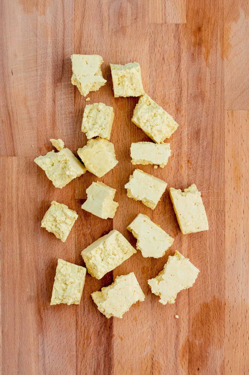 Teared tofu pieces on a wooden cutting board.
