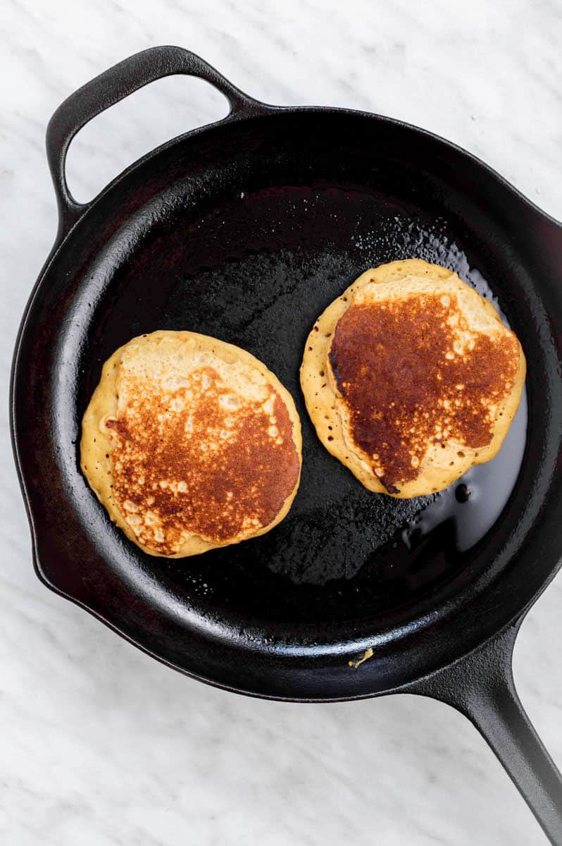 Two browned pancakes in a cast-iron skillet.