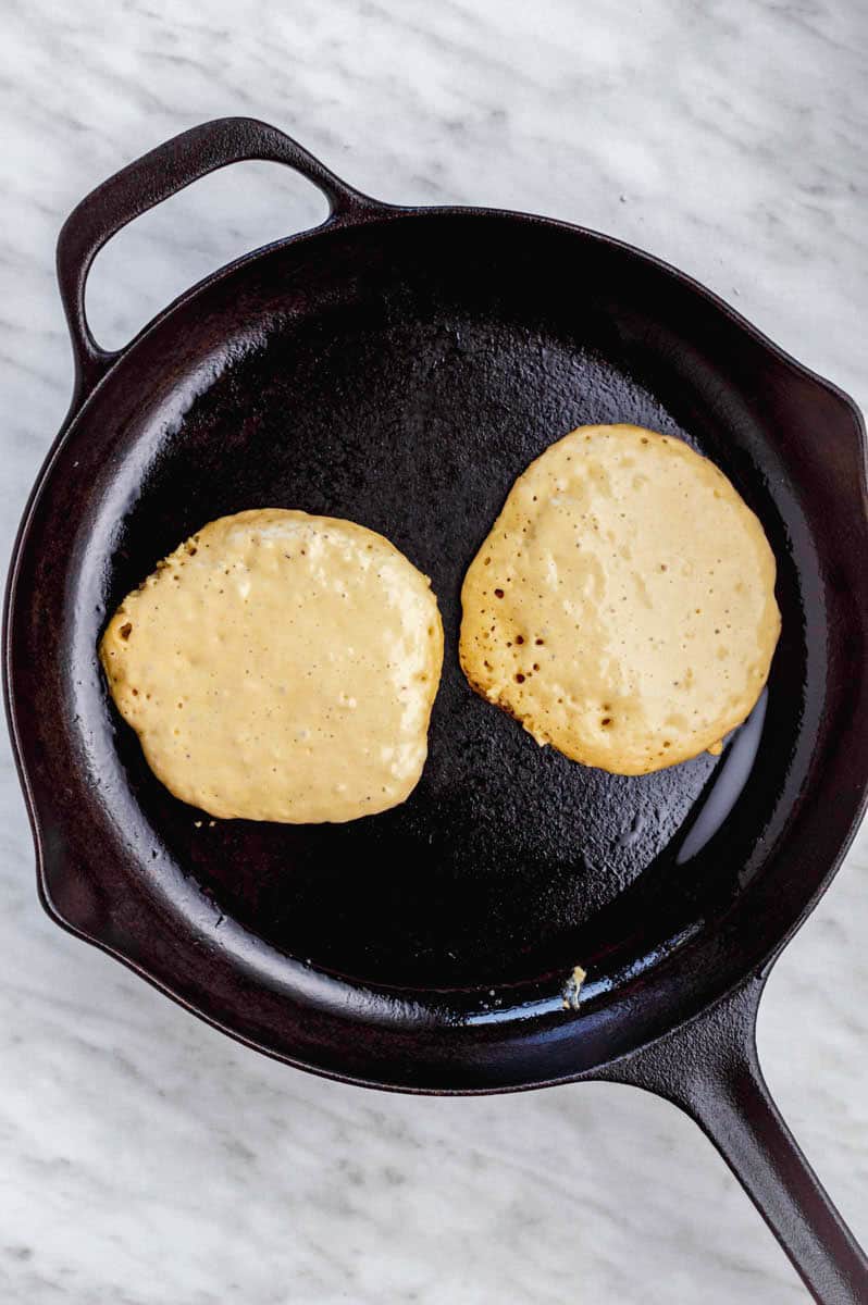 Cooking two pancakes in a cast-iron skillet.