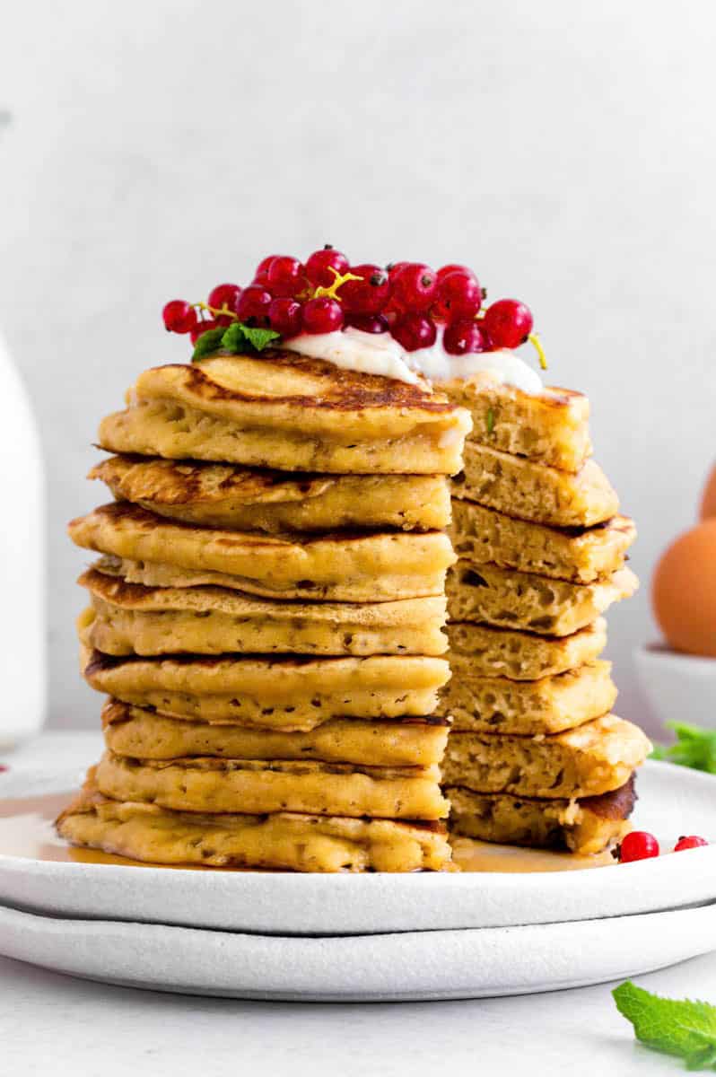 A stack of almond milk pancakes topped with red grapes and yogurt, with a part cut out of them.