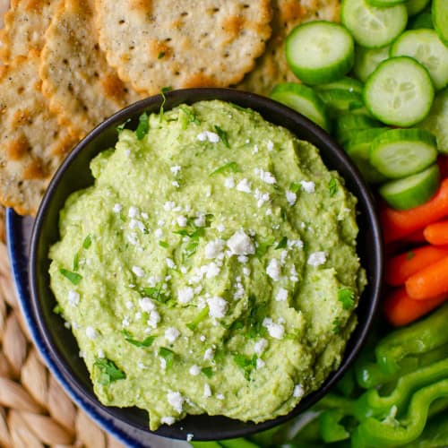 Avocado feta dip with vegetables and crackers on a dish.