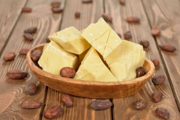 cocoa butter chunks in a dish with cocoa beans around it.