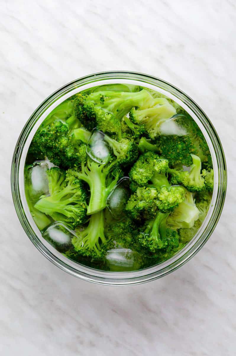 Blanched broccoli in ice water in a large bowl.