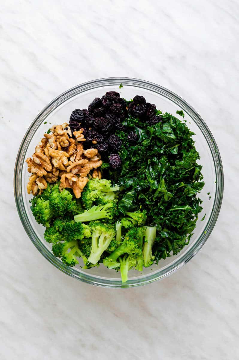 Massaged kale, walnuts, broccoli and dried cherries in a large mixing bowl.