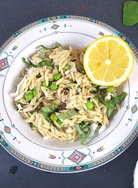 Creamy Orzo with lemon and peas served in a bowl with garnishes and lemon wedge.
