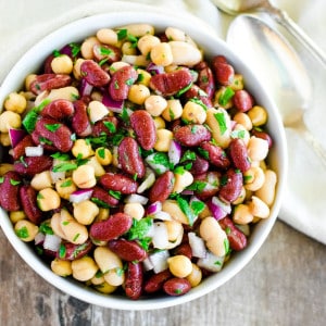 close-up of bean salad in a white bowl with spoons to the right.