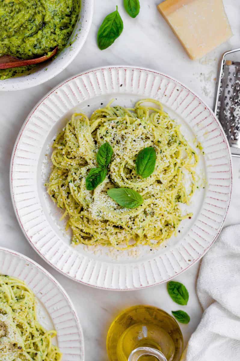 Pesto pasta served in a white bowl and topped with grated parmesan, black pepper and basil leaves.