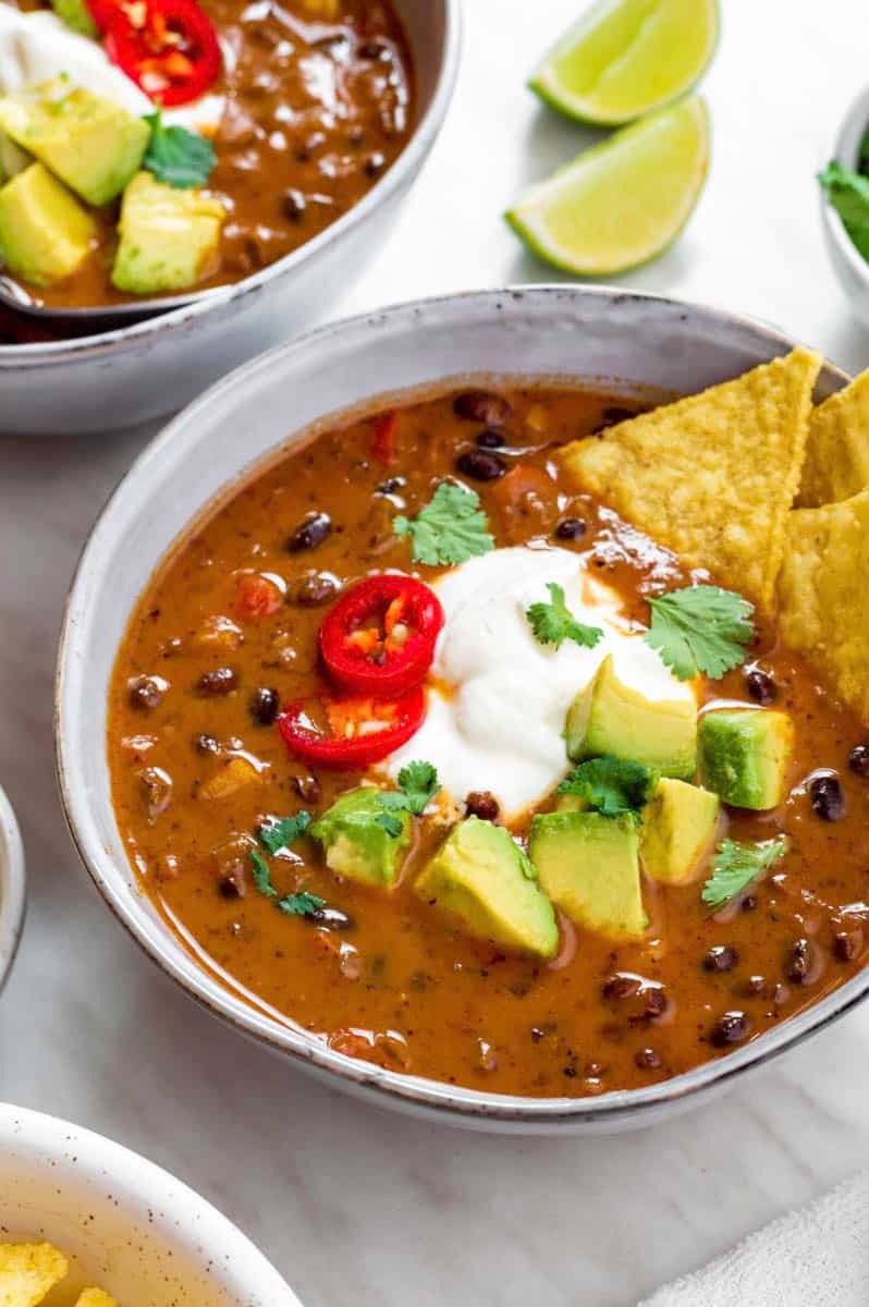 A blue bowl filled with Panera bread black bean soup topped with sour cream, avocado, cilantro and tortilla chips.