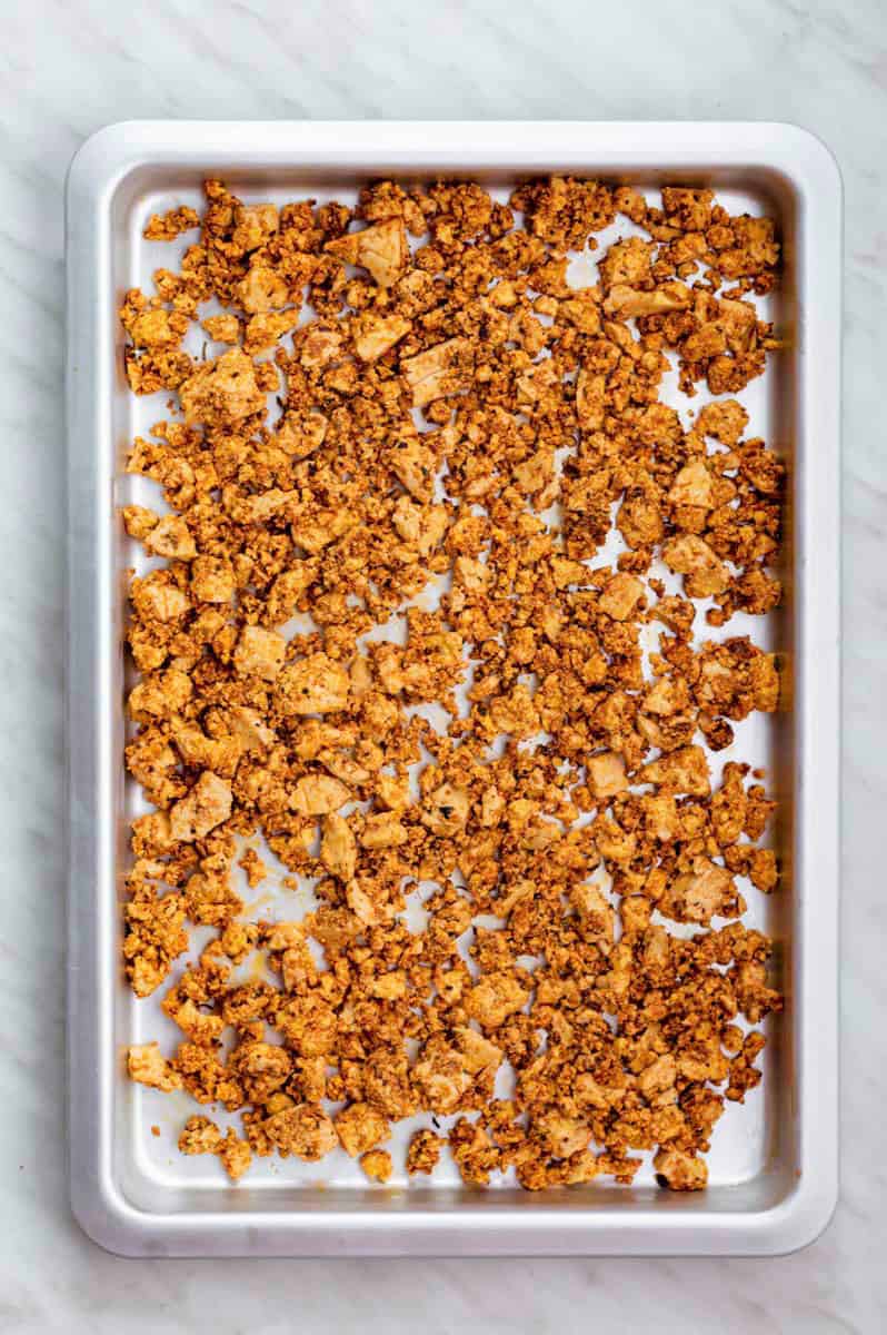 Crumbled tofu spread out on a stainless steel baking sheet.