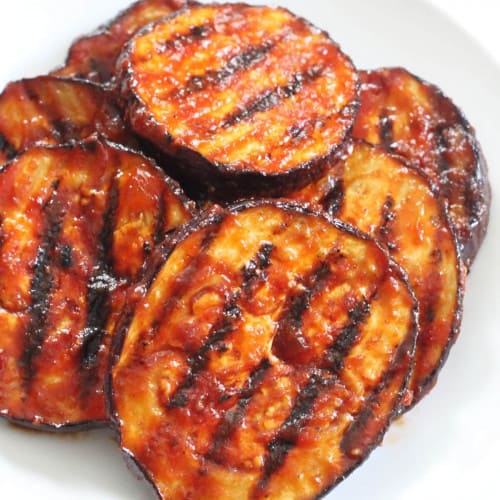 close-up of BBQ grilled eggplant on a white plate.