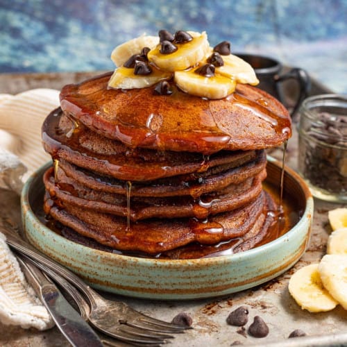 stack of chocolate banana pancakes with syrup oozing down.