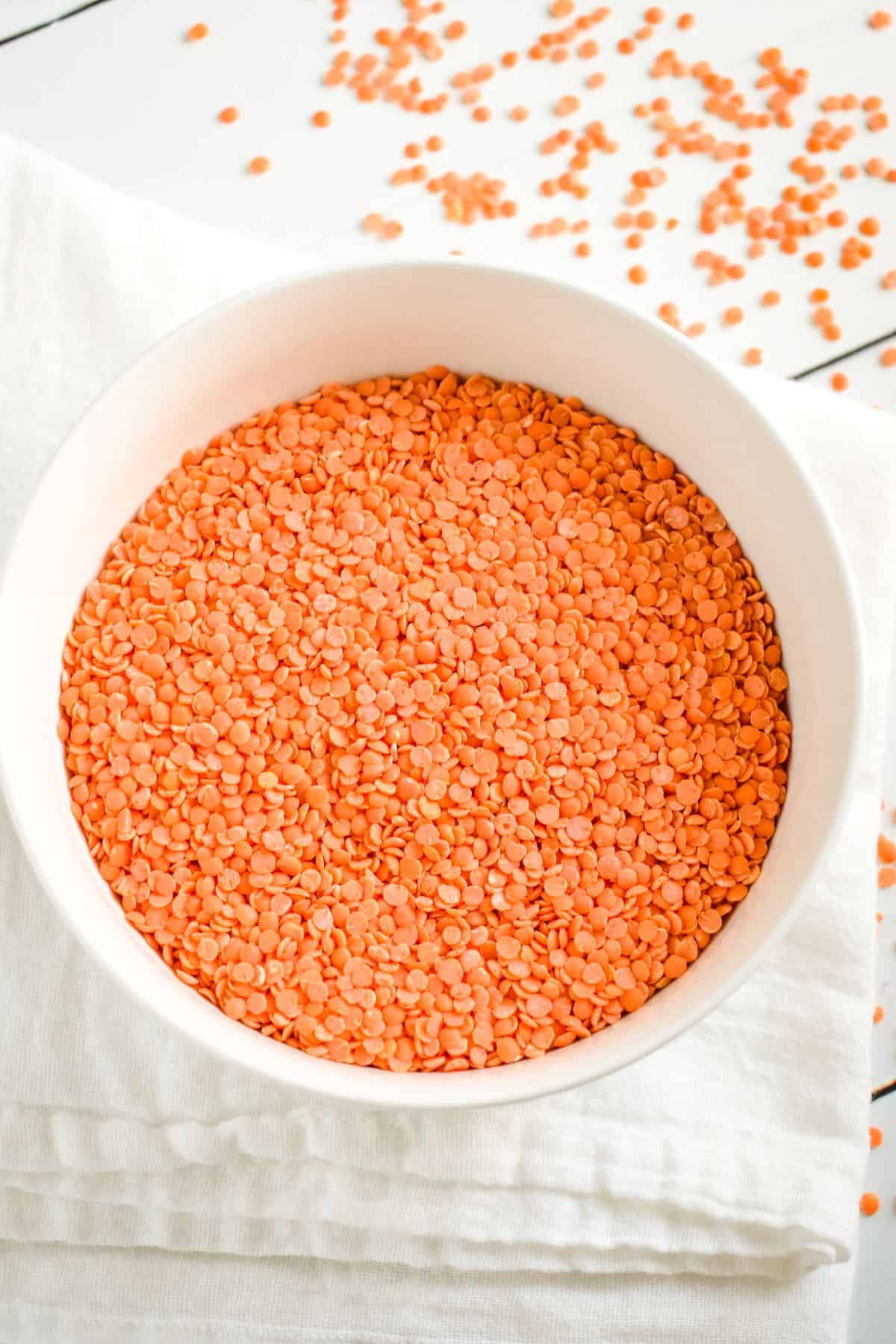 overhead of dry red lentils in a white bowl with some on the table behind it.