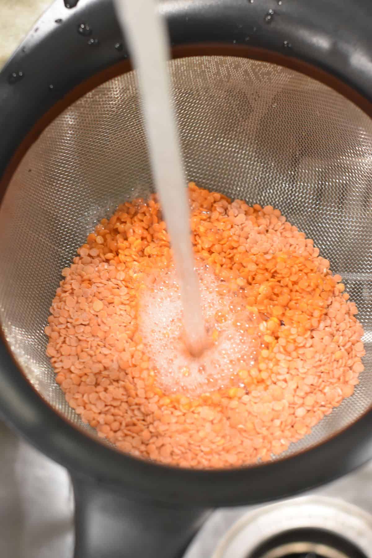 rinsing red lentils in a colander in the sink.