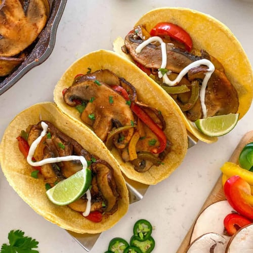 three mushroom fajitas in a taco holder with ingredients placed around.