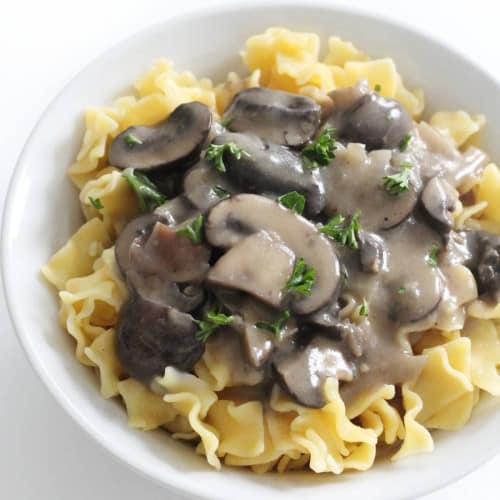 mushroom stroganoff on top of noodles in a white bowl.