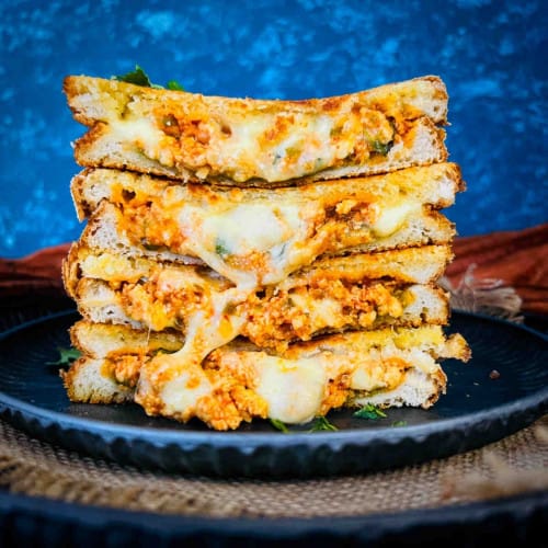 close up of four paneer sandwich halves stacked on top of each other with cheese dripping down.
