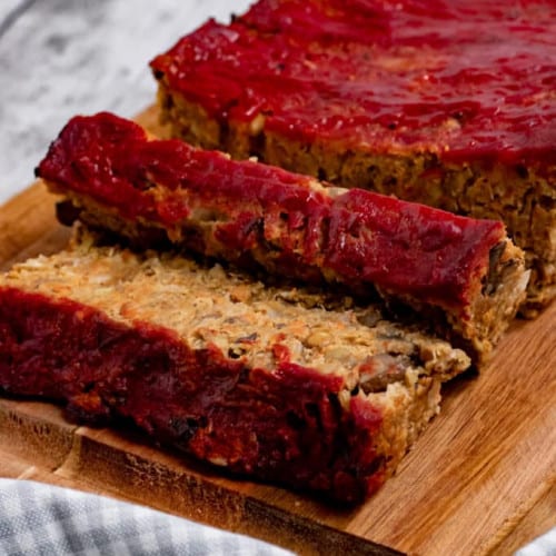 lentil loaf on a wooden board with two slices lying down in front.