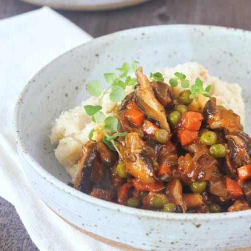 front view of vegan mushroom stew in a bowl with mashed potatoes.
