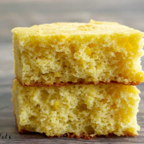 Two pieces of cornbread stacked on top of each other on a wooden surface.
