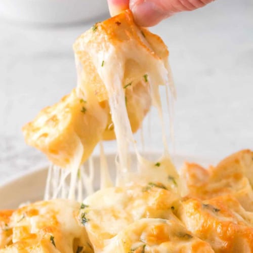 Hand pulling up a bite of cheesy garlic bread.