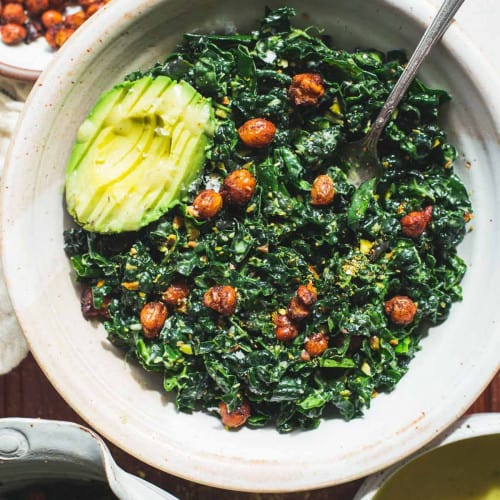 Kale and chickpea salad in a white bowl with a fork and sliced avocado.