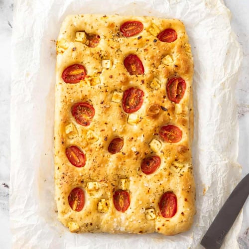 Focaccia topped with tomatoes on a piece of parchment.