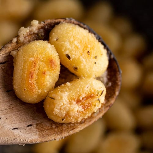 Three browned gnocchi in a wooden spoon.