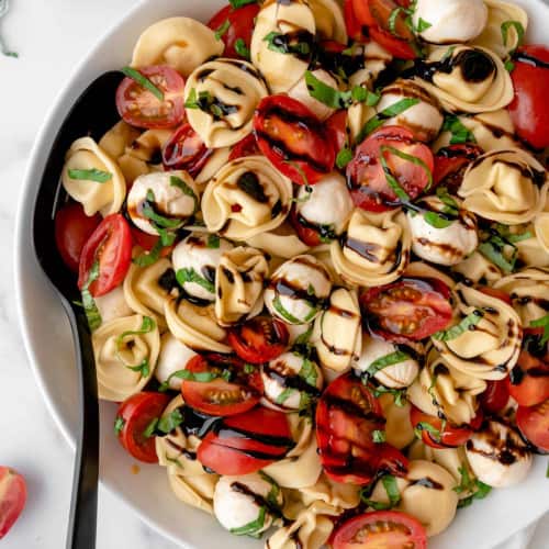 Tortellini salad in a bowl with tomatoes and balls of mozzarella.