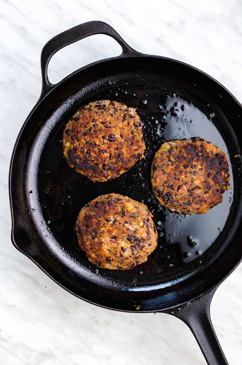 Three cooked black bean patties in a cast-iron skillet.