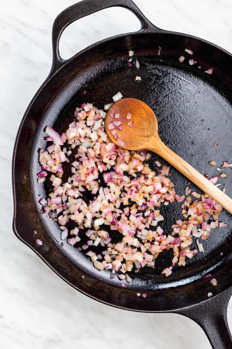 Sautéing red onion in a cast iron skillet with a wooden spoon in it.