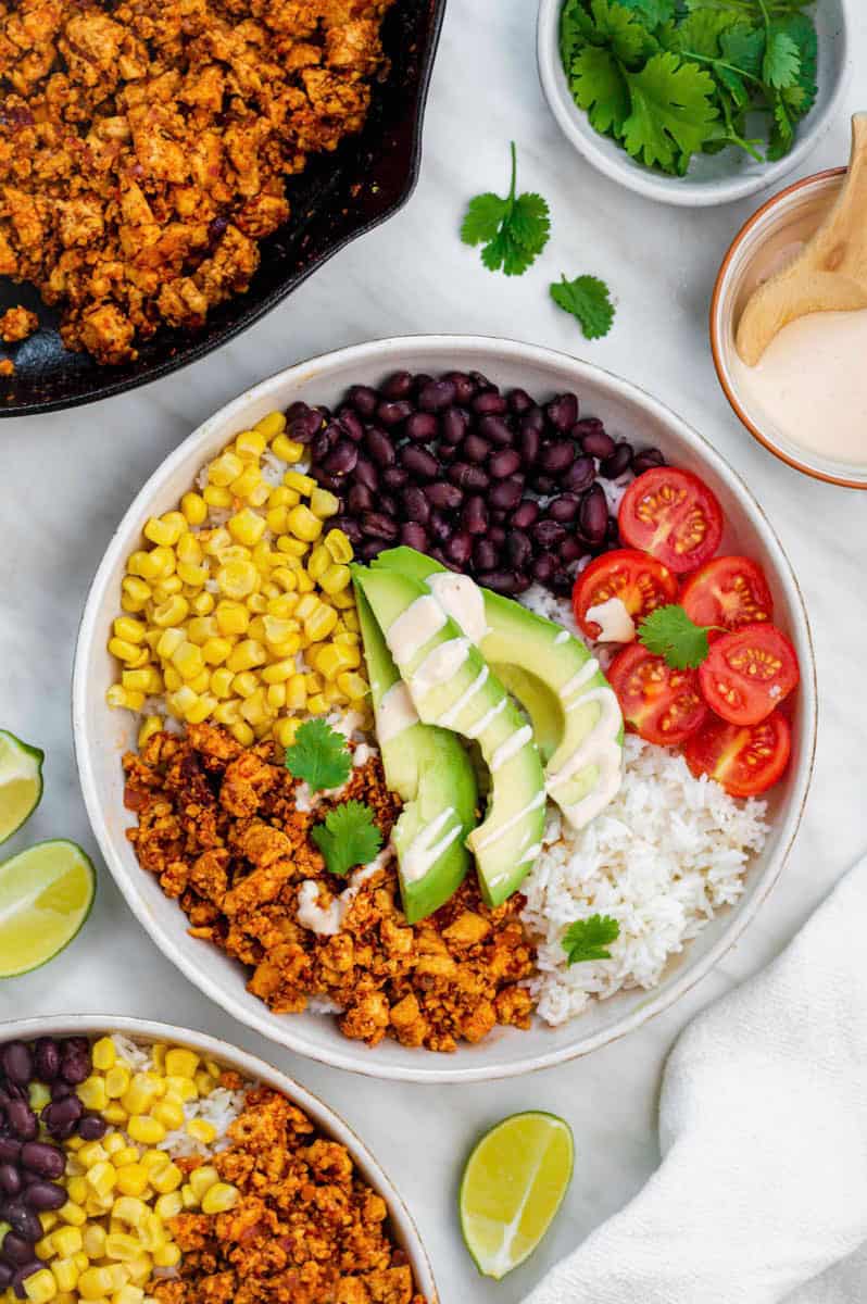Chipotle Plant-Based Sofritas served in a white plate with rice, avocado, black beans, corn, and cherry tomatoes.