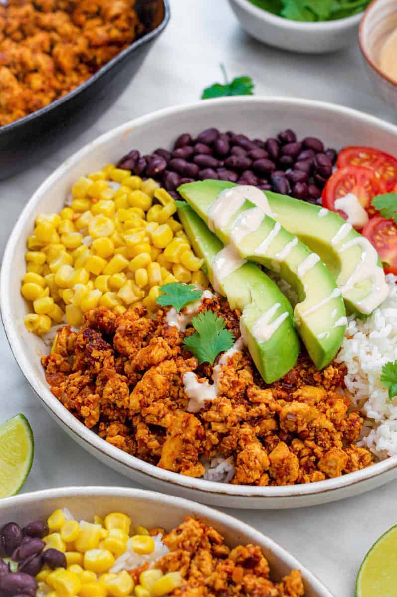 A white plate filled with Chipotle Plant-Based Sofritas served alongside rice, avocado, black beans, corn, and cherry tomatoes. 