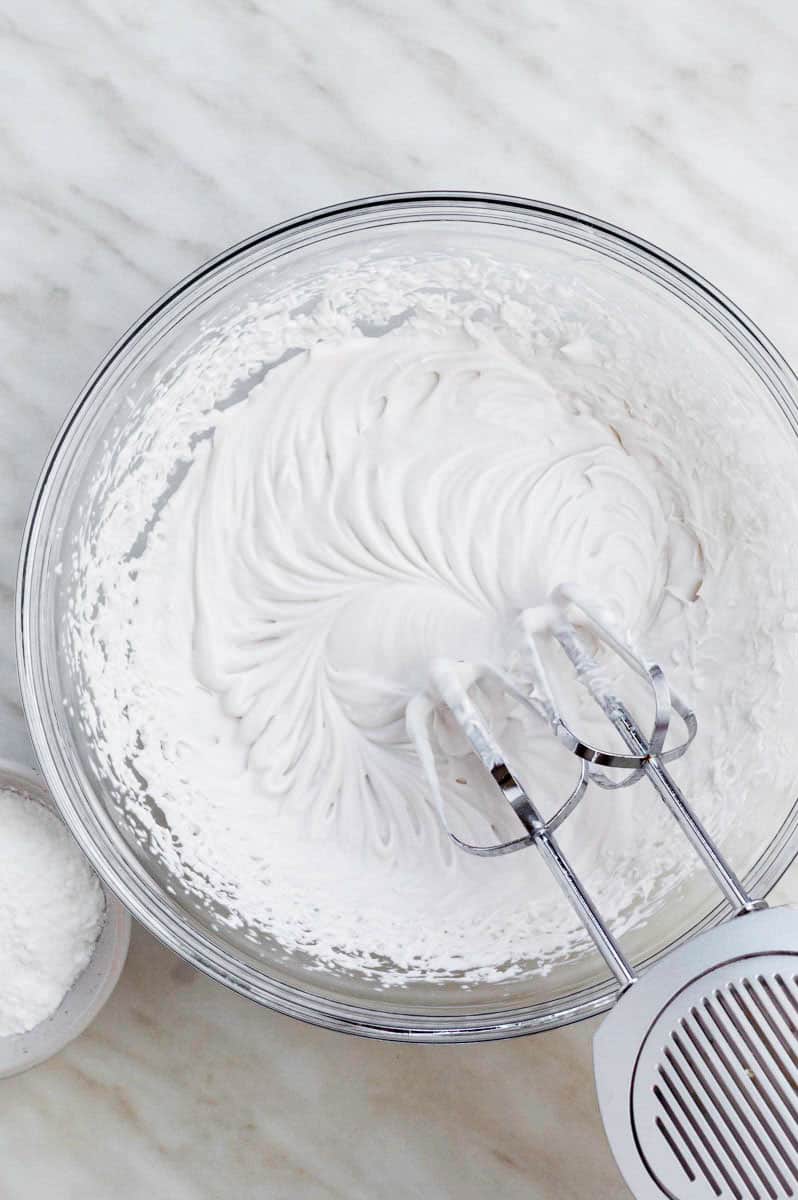 Beating coconut cream in a mixing bowl with an electric handheld mixer.