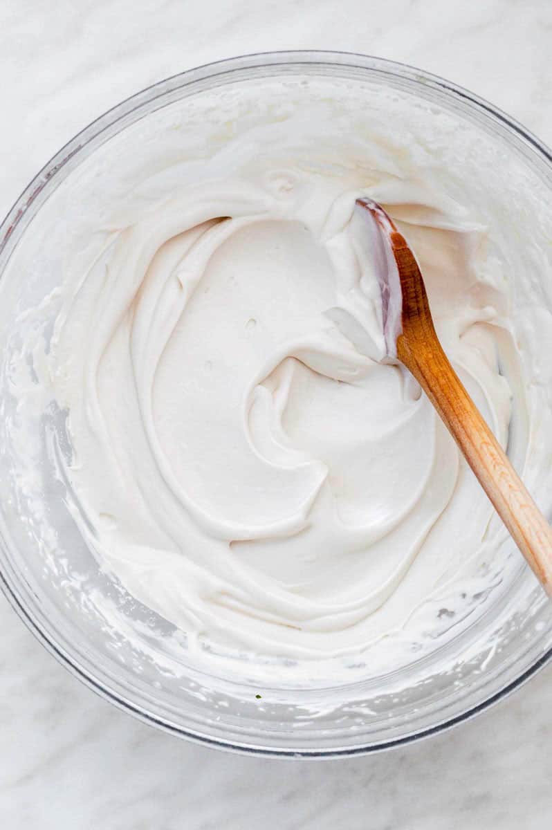 Dairy-free whipped cream in a mixing bowl with a wooden spoon in it.