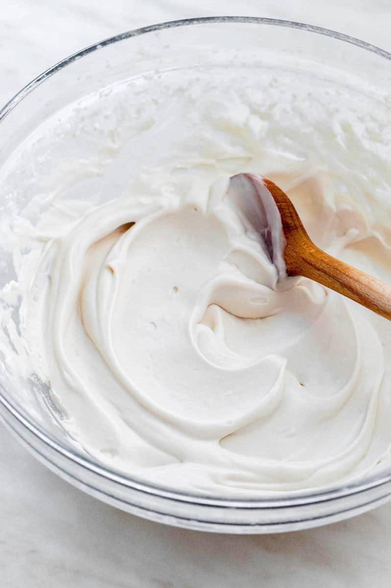 A mixing bowl filled with dairy-free whipped cream with a wooden spoon in it.