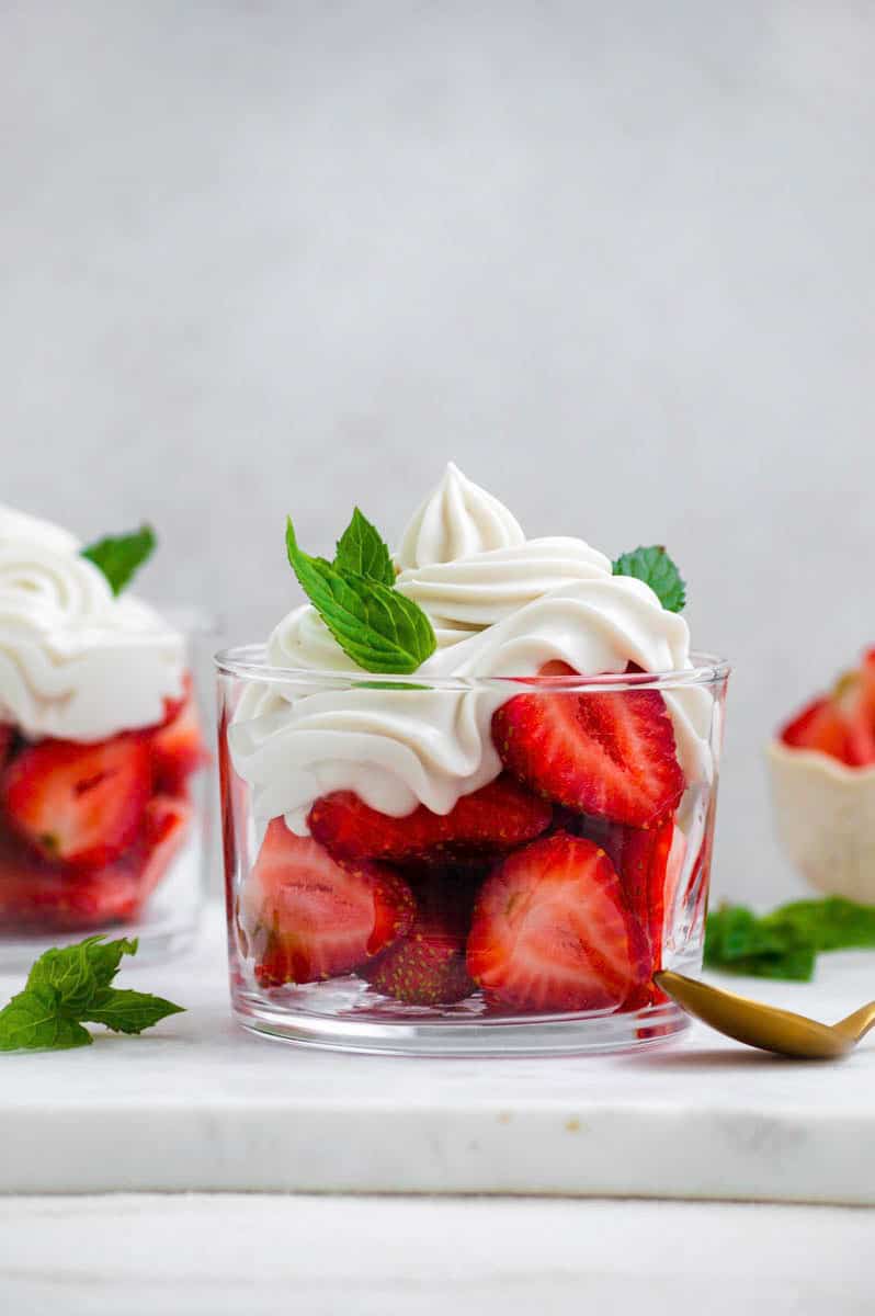 A small glass cup filled with halved strawberries topped with dairy-free whipped cream and fresh mint leaves.