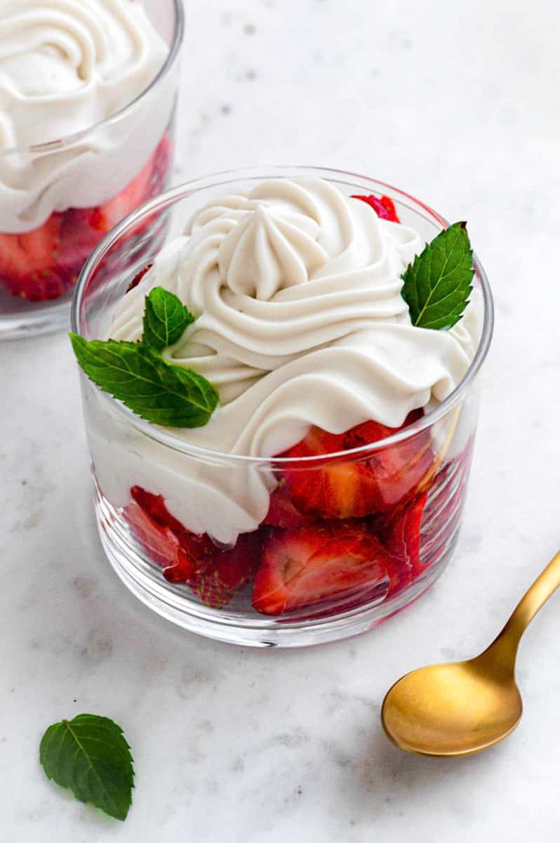 Top veiw of a glass cup filled with strawberries topped with dairy-free whipped cream and mint leaves.