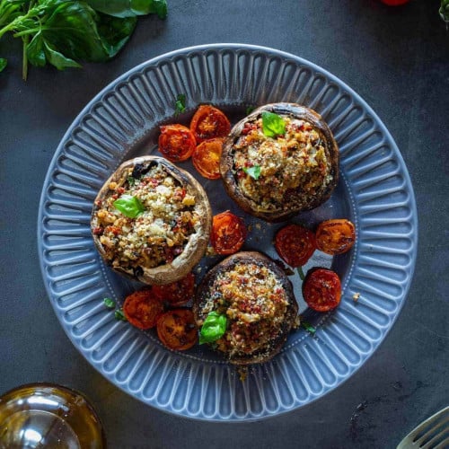 overhead of stuffed mushrooms on a plate with tomatoes around.
