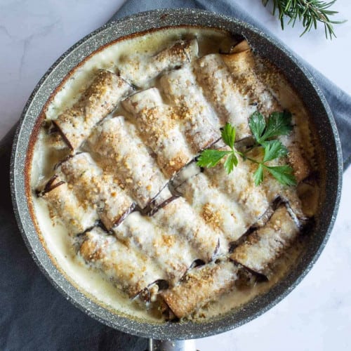 overhead of eggplant involtini in skillet on a kitchen towel.