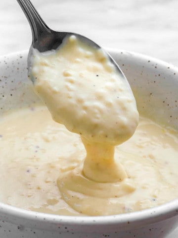A white bowl filled with garlic pizza sauce with a spoon dipping into it.
