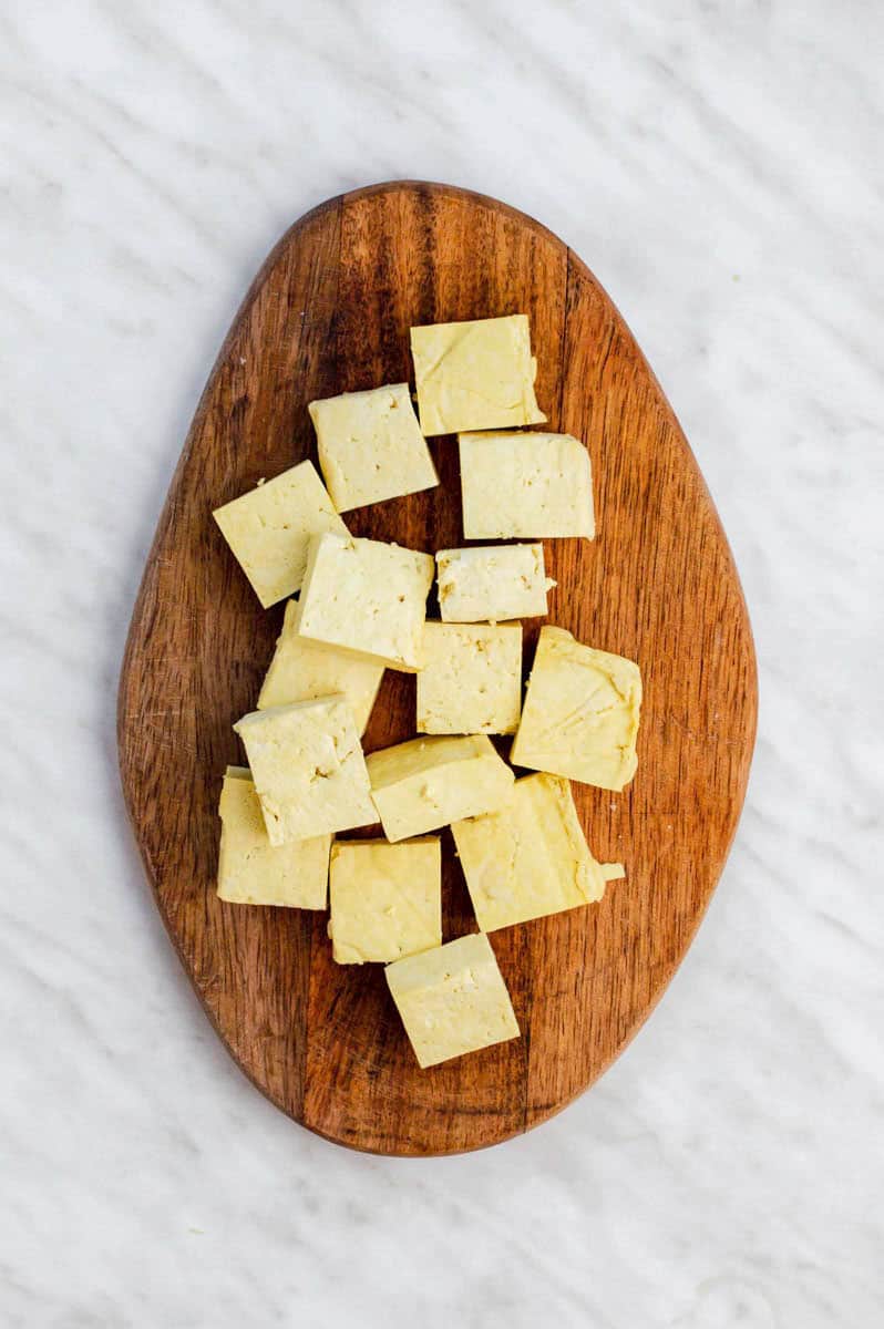 Tofu cubes on a wooden cutting board.