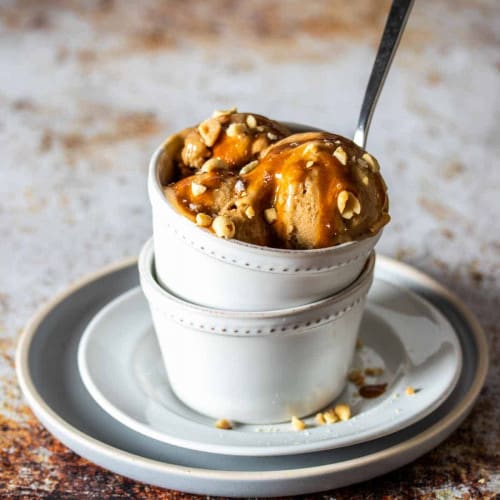 peanut butter banana nice cream in a bowl in anotehr bowl with peanut butter caramel topping and peanuts.