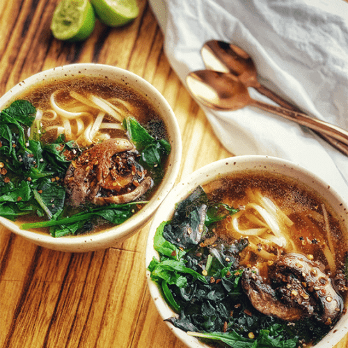 overhead of two bowls of pho soup with two spoons bheind them.